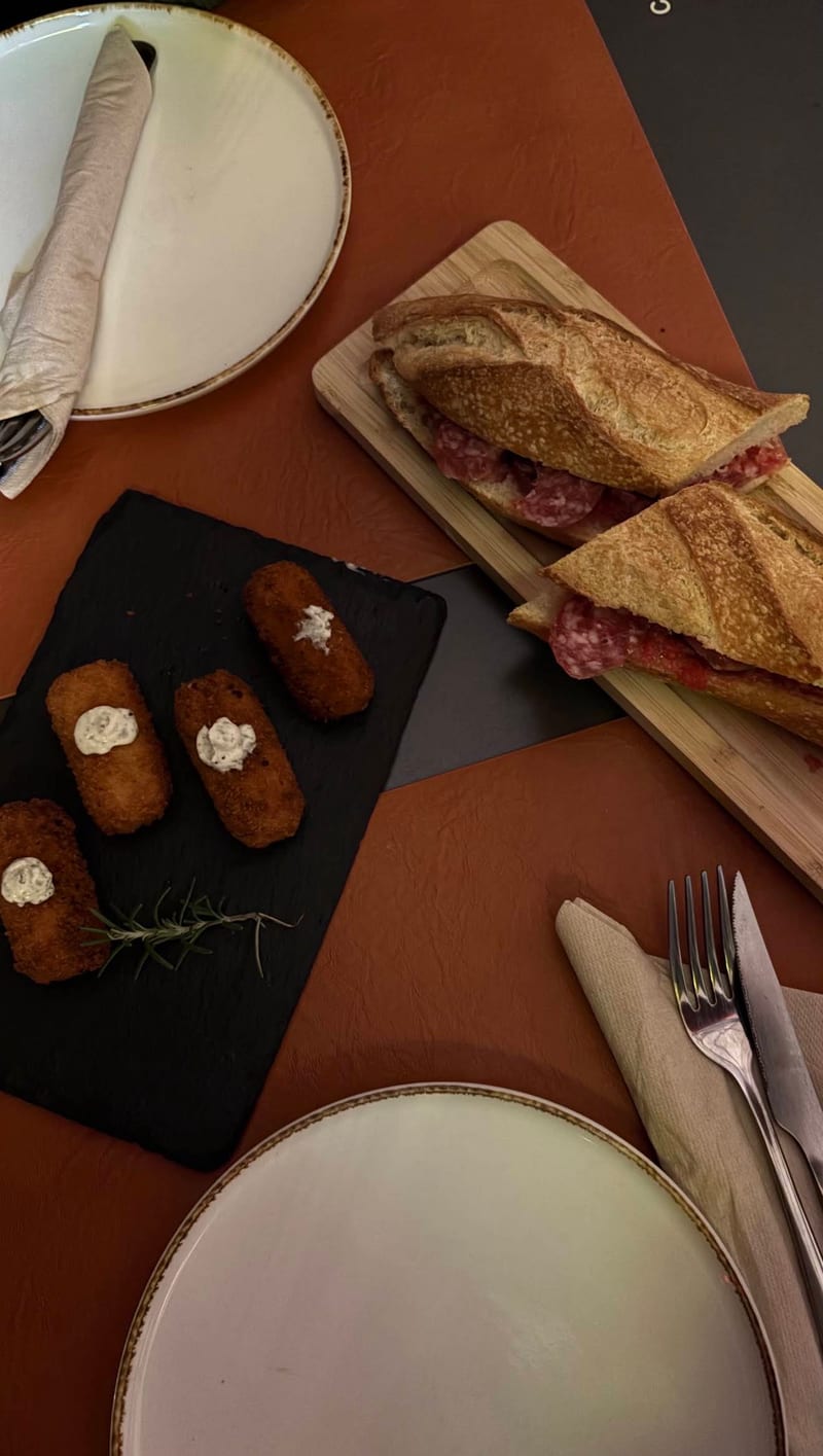 Croquetas en una pizarra y un bocadillo en una tabla, vistos desde arriba sobre la mesa