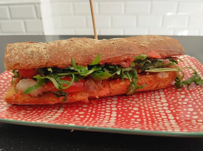Bocadillo con rúcula y tomate sobre un plato rojo con lunares