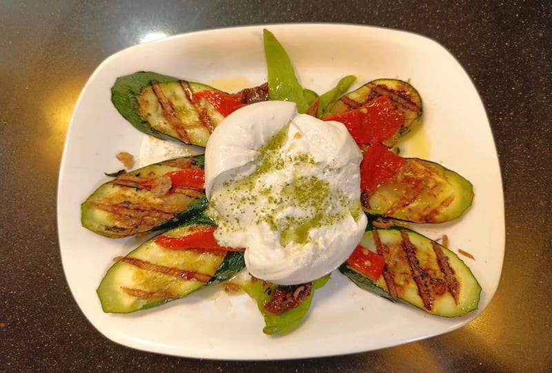 Burrata sobre verduras a la brasa en un plato blanco