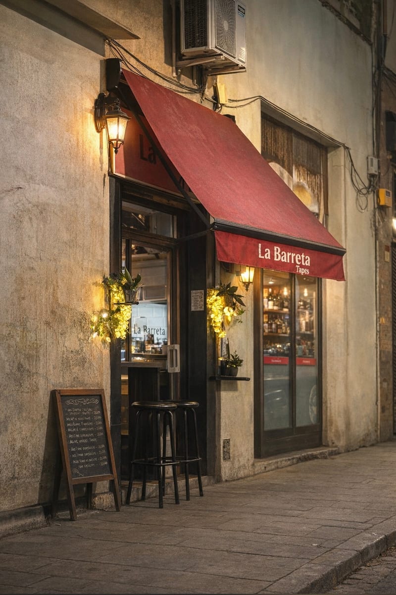 Fachada con toldo rojo de La Barreta, farol y taburetes en la acera